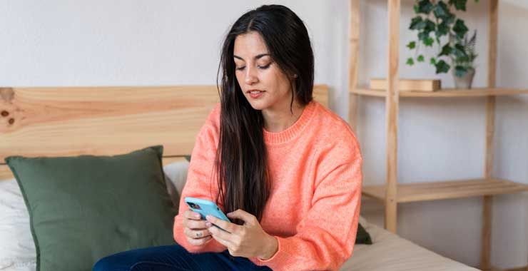 A woman sitting on her bed, looking at her smartphone